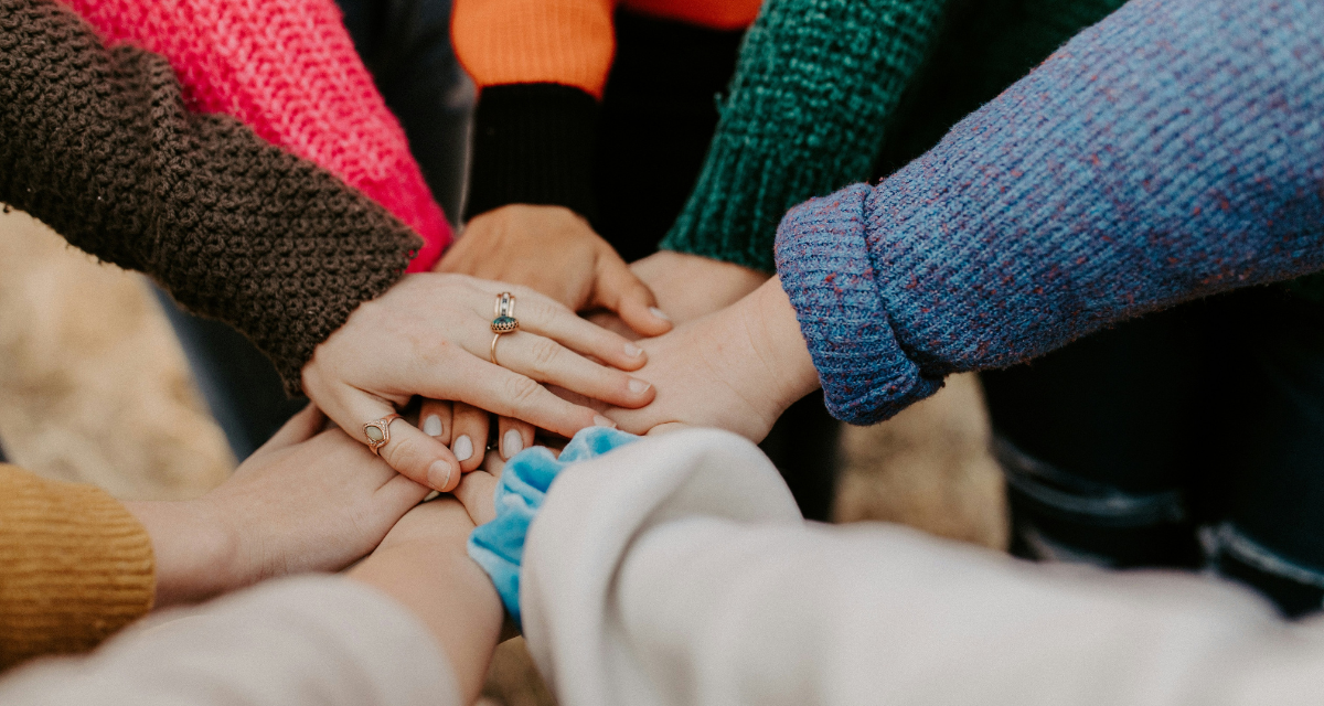 Gruppe stapelt Hände in bunte Pullover. Foto: Hannah Busing | Unsplash Gruppe stapelt Hände in bunte Pullover. Foto: Hannah Busing | Unsplash